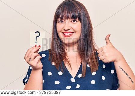 Young plus size woman holding question mark smiling happy and positive, thumb up doing excellent and approval sign 