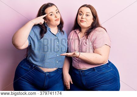 Young plus size twins wearing casual clothes confused and annoyed with open palm showing copy space and pointing finger to forehead. think about it. 