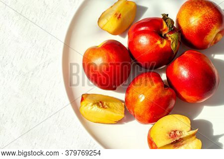 Red Ripe Organic Nectarine Fruits On The White Plate On Nature Background. Summertime Healthy Eating