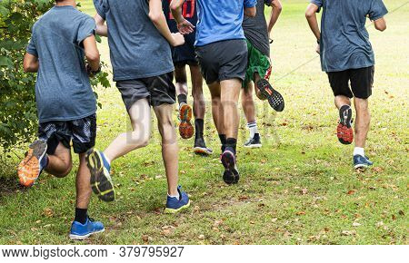 Rear View Of A Group Of High School Boys Training For Cross Country Running Grass In A Local Park.
