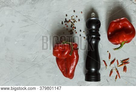 Two Shriveled Red Peppers, And A Pepper Mill On A Grey Rough Surface, Top View With Space