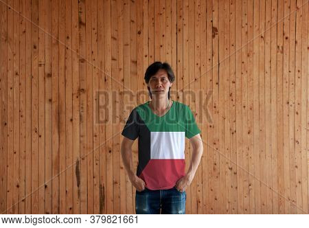 Man Wearing Kuwait Flag Color Shirt And Standing With Two Hands In Pant Pockets On The Wooden Wall B