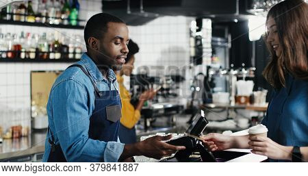 Multiethnic Bartender Man And Client Woman. Caucasian Female Paying With Paypass, Credit Card. Mixed