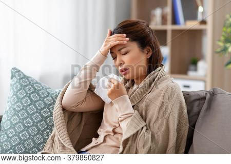 health, cold and people concept - sad sick young asian woman with paper tissue having headache at home
