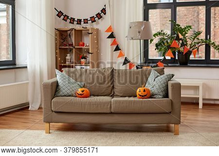 holidays, decoration and party concept - home room with jack-o-lanterns or pumpkins on sofa and halloween decorations