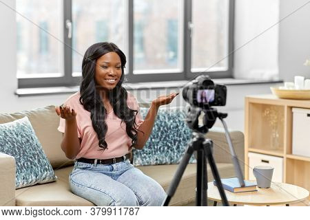 blogging, videoblog and people concept - happy smiling african american female video blogger with camera videoblogging at home