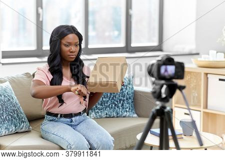 blogging, videoblog and people concept - african american female video blogger with parcel box and camera videoblogging at home