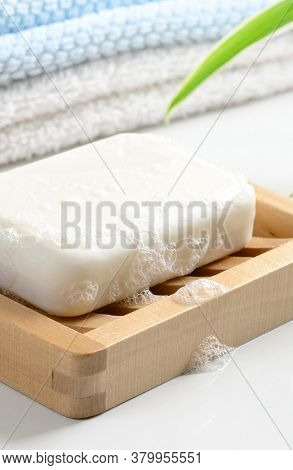 White Soap Bar With Foam On Wooden Soap Dish And Cotton Towels On White Counter Table In The Bathroo