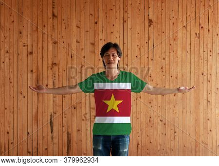 Man Wearing Suriname Flag Color Shirt And Standing With Arms Wide Open On The Wooden Wall Background