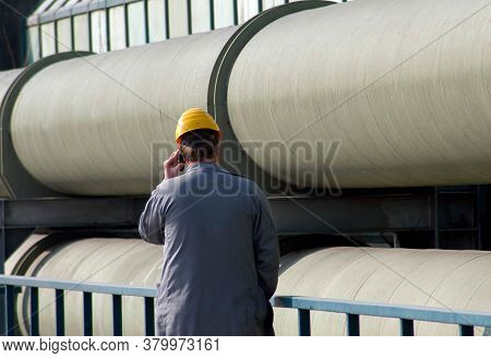 Man In Working Clothes On The Telephone In Front Of District Heating Pipelines For Heat Transportati