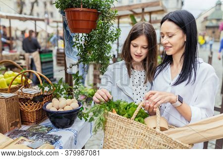 Two Sisiters Buying From An Organic Vegetable Stall At A Farmers Market, On A Sunny Morning, Young W