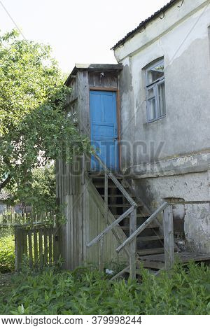 An Old Abandoned European Home With A Wooden Blue Door With A Closed Lock, Wooden Staircase And An U