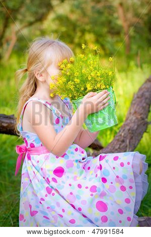 Little Girl Sitting On A Branch Of A Tree And Smelling The Flowers