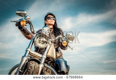 Biker girl in a leather jacket on a motorcycle looking at the sunset.