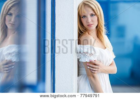 Young beautiful blond woman in white dress near the office building
