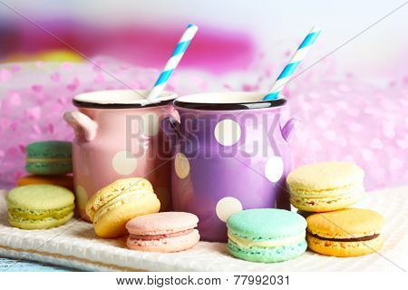 Gentle colorful macaroons and milk in decorative mugs on color wooden background