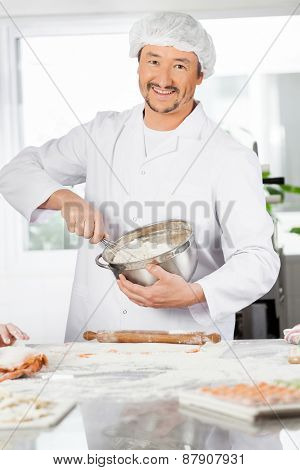 Portrait of happy male chef mixing batter in bowl to prepare ravioli pasta in commercial kitchen