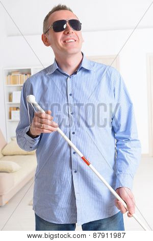 Blind man with white stick and dark glasses at home