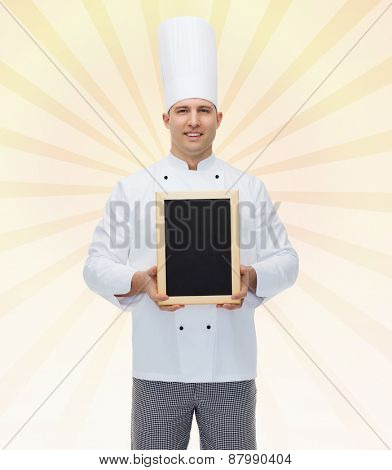 cooking, profession, advertisement and people concept - happy male chef cook showing and holding blank menu board over yellow burst rays background