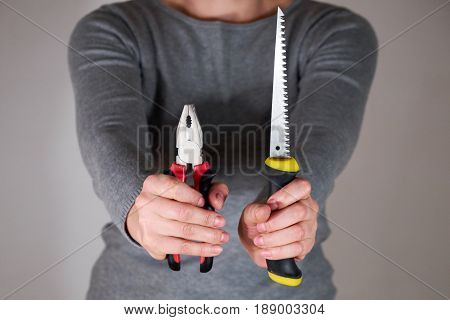 Woman holding pliers and saw in two hands