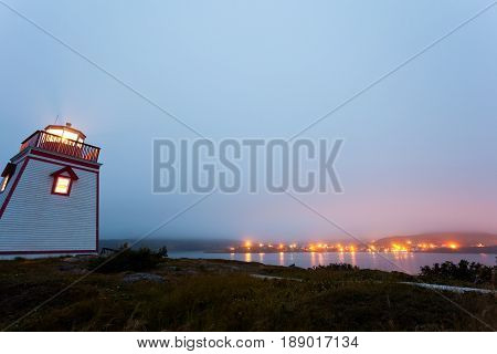 Foggy twilight at lighthouse on Fort Point with village of Trinity in the distance Newfoundland NL Canada