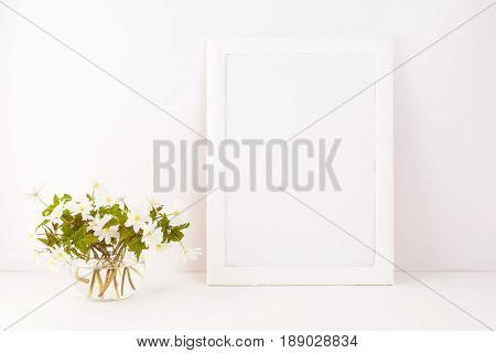 White frame mockup with blooming Rue Anemone. Empty frame mock up for presentation artwork. Template framing for modern art.