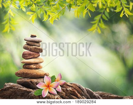 Spa background concept. Pile of small stone as pyramid and pink plumeria flower over green anstract background