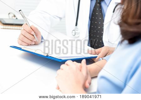 Doctor talking note on clipboard while consulting with woman patient -medical consultation and examination concepts