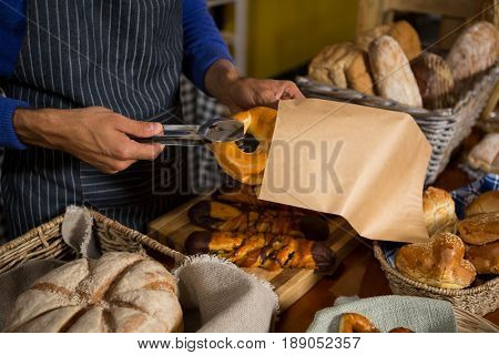 Mid section of staff packing croissant in paper bag at counter in bakery shop