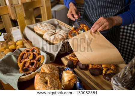 Mid section of staff packing croissant in paper bag at counter in bakery shop