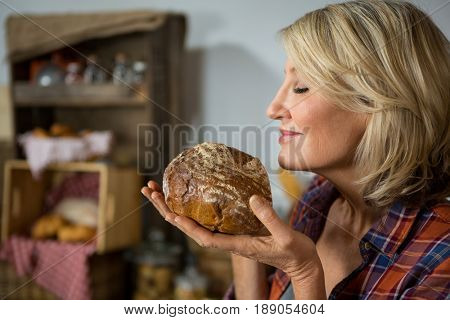 Smiling woman smelling a round loaf of bread at counter in bake shop