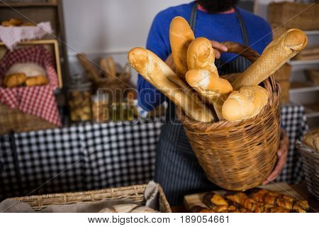 Mid section of staff holding wicker basket of french breads at counter in bakery shop