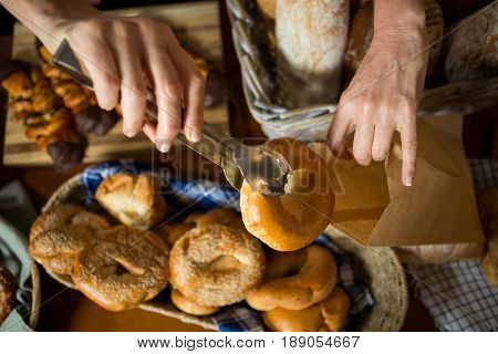 Mid section of staff packing doughnut in paper bag at counter in bakery shop