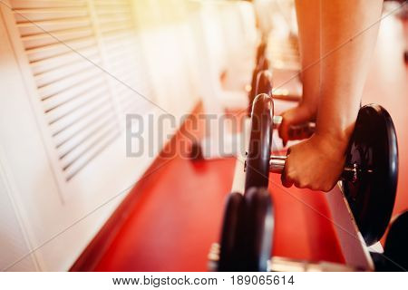 Sports equipment dumbbell rests in a row, girl takes a dumbbell in the gym. hands close-up. hign contrast and monochrome color tone