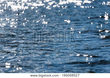 Water bokeh background. Defocused water surface with waves glittering in the sun.