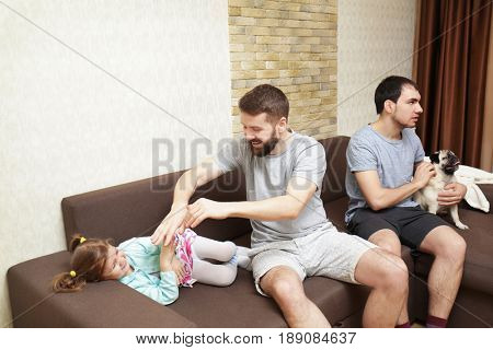 Male gay couple with little girl sitting on sofa at home