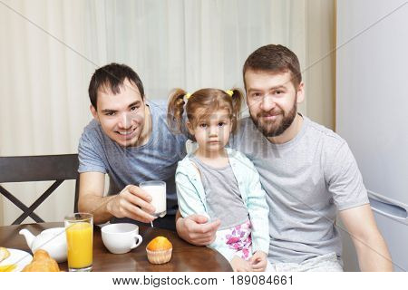 Male gay couple with daughter having breakfast in kitchen