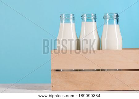 Glass Bottles With Milk In Wooden Box On Tabletop At Blue Background