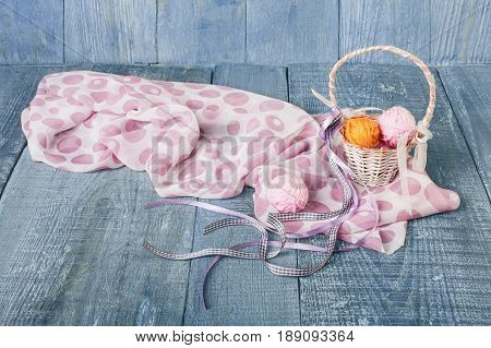Yarn balls in basket. Knitwork background. Art craft, hand made. Handiwork, knitting, sewing, needlework. Wicker basket with woolen pink and orange balls and silk scarf at blue rustic wood background