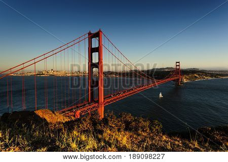 A little boat sails underneath the Golden Gate Bridge, San Francsico, during sunet.