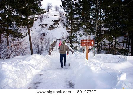 Father carries his baby daughter on a snow-covered interpretive trail at Lone Pine State Park, Kalispell, Montana