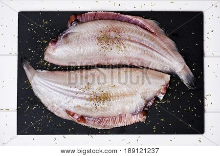 high-angle shot of a pair f raw filleted common sole on a slate tray placed on a rustic wooden table
