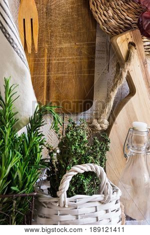 Provence style kitchen interior white wooden wall cutting board utensils rattan coaster linen towel fresh garden herbs rosemary thyme glass bottle dried peppers on string
