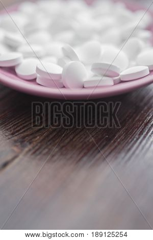 Large white pills on a small bright pink plate on a dark brown wooden background at the top of the frame.