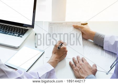 Two doctors being discussing patient history in an office pointing to a clipboard with document paper as they make a diagnosis or recommend on treatment.