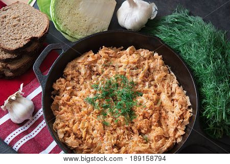 Delicious stewed cabbage in iron pan on dark rustic background with the ingredients for this dish. vegetarian food