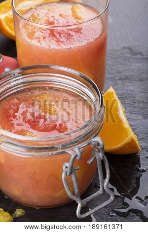 Citrus jelly in a glass jar on a black slate background. Homemade grapefruit orange gelatin dessert. Healthy low fat and low calorie meal.
