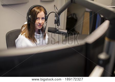 Portrait of young female host wearing headphones while communicating on microphone in radio studio