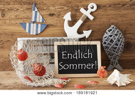 Blackboard With Nautical Summer Decoration And Wooden Background. German Text Endlich Sommer Means Hello Summer. Fish, Anchor, Shells And Fishnet For Maritime Contex.