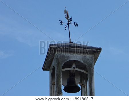 A weather-vane and bell against a crisp blue sky.
